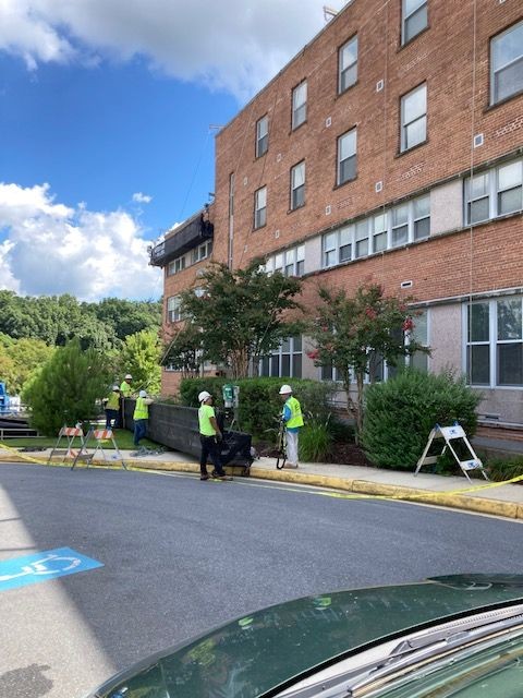 Photo of five construction workers in hi-viz work vests and hardhats, working on the brick exterior of St. Ann's Center.